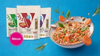Nieuw assortiment AH Maaltijdverrijkers in de smaken Mediterraan, Chili en Knoflook & ui, afgebeeld naast een kleurrijke maaltijdsalade met groenten en noten op een blauwe achtergrond.