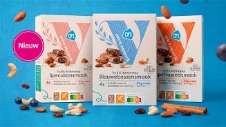 Drie verpakkingen Albert Heijn Fruit & Notenrepen in de smaken speculaas, blauwe bes en appel-kaneel, omringd door noten, gedroogd fruit en een label “Nieuw” op een blauwe achtergrond.