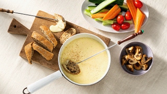 Fondue met gesmolten kaas, stokbrood, groenten en champignons op tafel.