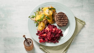 Gerecht met gegrilde hamburger, gebakken aardappelschijfjes met rucola, en rode bietensalade op een bord.
