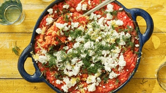 Eenpan roerbak met tomatensaus, versierd met feta kaas en dille, geserveerd op een houten tafel.