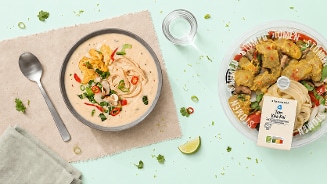 Tom Kha Kai stoomsoep van Albert Heijn, geserveerd met soep, noodles en groente in een kom, naast de verpakking met verse ingrediënten.