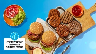 Twee hamburgers met sesambroodjes, sla en uien liggen op een plank, naast vier gegrilde burgerpatty’s op een bakplaat en een schaaltje ketchup. Links een bord met sla, tomaat en uien, en een sticker met de tekst "Prijsfavorieten - Topkwaliteit. Altijd laag geprijsd." op een blauwe achtergrond.