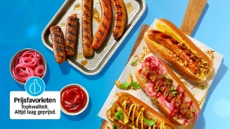 Grillworsten en hotdogs, geserveerd op een bakplaat en op broodjes met verschillende toppings zoals zoetzure rode ui, ketchup, mosterd en groene kruiden. Op de achtergrond een "Prijsfavorieten" label van Albert Heijn.