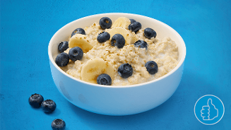 Havermoutpap met plakjes banaan en blauwe bessen in een witte kom op een blauwe achtergrond