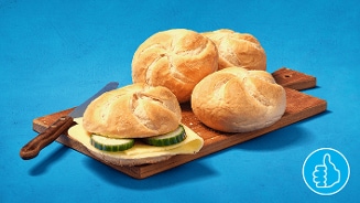 Kaiserbroodjes op een houten plank, één belegd met kaas en komkommer, op een blauwe achtergrond