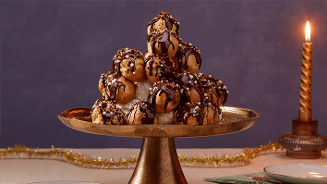 Soezentoren van slagroomsoesjes met chocoladesaus op een gouden etagère, feestelijk gepresenteerd naast een brandende kaars