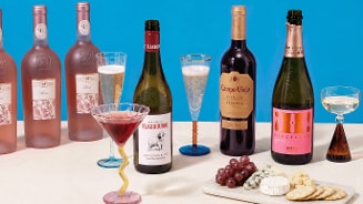 Verschillende flessen wijn, waaronder Campo Viejo Rioja Reserva en Flaxbourne Sauvignon Blanc, met bijpassende glazen wijn en bruisende drankjes op een tafel, naast een tros rode druiven.