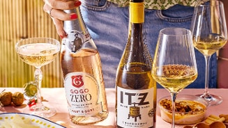 Flessen en glazen met GoGo Zero Sparkling Rosé en ITZ Chardonnay wijn op een gedekte tafel, samen met borrelhapjes.