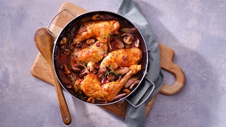 Kipstoofpot met champignons en kruiden in een pan op een houten snijplank.