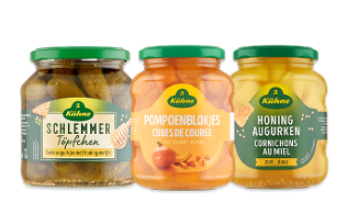 Drie potten Kühne producten: zoete augurkjes, pompoenblokjes en honing augurken, elk met groene deksel en label, op een transparante achtergrond.