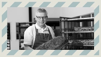 Bakker met ovenhandschoenen houdt versgebakken brood vast in een bakkerij.