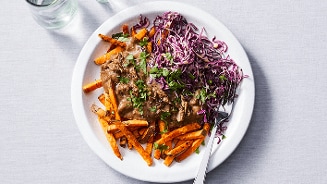 Bord met zoete aardappelfriet, rundvlees gerecht en rode kool slaw.