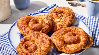 Vier versgebakken koffiebroodjes op een blauw-wit bord met een blauw geruit servet, klaar om geserveerd te worden.
