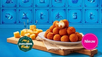 Stukjes Zaanlander kaas en een bord met kaasballetjes op een houten plank, tegen een decoratieve blauwe tegelachtergrond. Het product is nieuw.