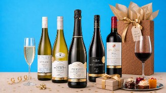 Verschillende flessen wijn waaronder Riesling, Chardonnay, Prosecco, Spätburgunder en Rioja, samen met een glas witte en rode wijn, cadeautjes en een feestelijke geschenkverpakking, op een gedecoreerde tafel met hapjes tegen een blauwe achtergrond.