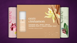 Care Cozy Cinnamon giftset met showergel, bodycrème, douchepuff, haar- en bodymist met kaneel, vanille en ceder, geflankeerd door Care cherry blossom en botanical sage geurstokjes