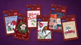 Verschillende Hallmark kerstkaarten met feestelijke ontwerpen zoals kerstcadeaus, een kat met kerstmuts, een roodborstje, kerstgroet en kerstboom op auto, tegen een paarse achtergrond.