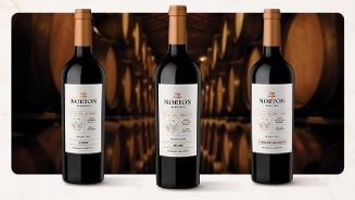 Drie flessen Norton Barrel Select rode wijn, met varianten Merlot, Malbec en Cabernet Sauvignon, gepresenteerd voor een achtergrond van wijnvaten in een wijnkelder
