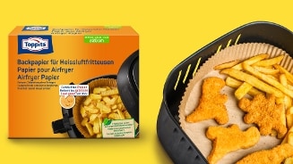 Verpakking Toppits Airfryer Papier 20 cm afgebeeld naast een airfryer mand met bakpapier, frietjes en kipnuggets op een gele achtergrond