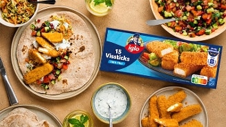 Een tafelsetting met verschillende borden met wraps, frisse salade, yoghurtsaus en een bord met krokante Iglo vissticks. In het midden ligt een verpakking van Iglo 15 vissticks.