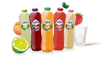 Vijf flessen Spa Fruit frisdrank in verschillende smaken (lime ginger, strawberry blackcurrant, mango apricot, strawberry lemonade, peach pear) staan naast bijpassend fruit en een glas.
