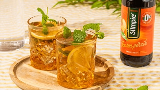 Twee glazen ijsthee met citroen en munt op een houten dienblad, naast een fles Slimpie Ice Tea perzik siroop.