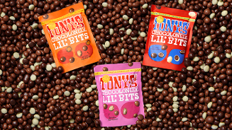 Drie verpakkingen van Tony's Chocolonely Lil' Bits in verschillende smaken, op een achtergrond van chocoladestukjes.