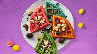 Kleurrijke wafels met paaseitjes op een wit bord, gepresenteerd op een paarse ondergrond met paaseitjes en decoratieve items