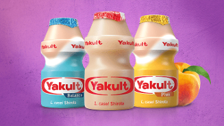 Drie Yakult flesjes, varianten Balance, Original en Plus, staan naast elkaar op een paarse achtergrond, met een perzik rechts van de Yakult Plus fles.