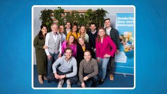 Groepsfoto van mensen voor een groene plantenwand, met een reclamebord van Albert Heijn met de tekst "Boodschappen doen wordt kinderspel".
