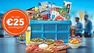 Borrelpakket met verschillende snacks, kaasblokjes met Nederlandse vlagprikkers, dranken en bekende merken zoals Doritos, Heineken en Red Bull in een blauwe Albert Heijn krat, samen met een ronde sticker met de tekst "Nu met €25 borreltegoed".