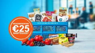 Blauwe Albert Heijn winkelmand gevuld met diverse producten, zoals AH granola bites, snack a jacks, fruit, repen, yoghurt en AH ovenkrokante sticks. Op de voorgrond verschillende soorten fruit waaronder appels, aardbeien en blauwe bessen. Links een oranje cirkel met de tekst "Welkomstkorting €25 shoptegoed".