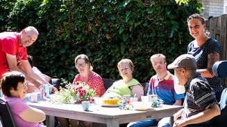 Mensen genieten van een sociale bijeenkomst aan een buitentafel omringd door groen.