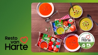 Twee maaltijdpakketten voor soep liggen op een houten tafel, omringd door kommen met rode en gele soep. In de pakketten zitten onder meer tomaten, ui, prei en kruiden. Op beide verpakkingen staat een kleine sticker met de tekst: “Hart voor elkaar”. Rechtsonder staat een grote wit-groene cirkel met de tekst: “Albert Heijn en Postcode Loterij doneren €0,50 van dit verspakket aan”, “RESTO van Harte”, “Zodat iedereen kan aanschuiven”, “ah” en “POSTCODE LOTERIJ”.