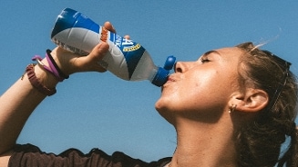 Persoon drinkt uit een fles Campina melk tegen blauwe lucht