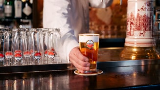 Glas Amstel bier wordt door een medewerker op een bar geplaatst, met Amstel bierglazen en een biertap op de achtergrond.
