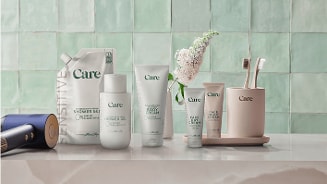 Care verzorgingsproducten en tandenborstelset op een badkamerblad met groene tegelmuur op de achtergrond