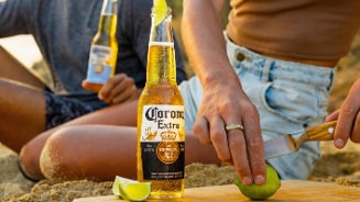 Fles Corona Extra bier op het strand met mensen die limoen snijden en bier drinken