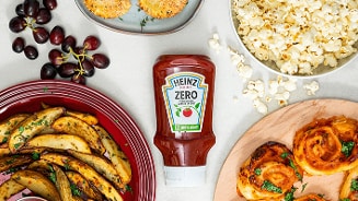 Heinz Zero Tomaten Ketchup omringd door diverse snacks zoals aardappelwedges, popcorn, druiven en hartige broodjes.