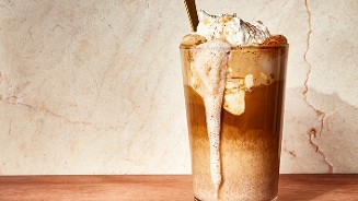 IJskoffie met slagroom in een glas met een lepel, op een houten ondergrond