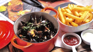 Mosselen in een rode pan met een portie friet op de achtergrond