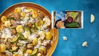 Gerecht met gnocchi, courgette, bloemkool, ui en geraspte kaas op een bord, met daarnaast een Allerhande maaltijdpakket van Albert Heijn met ingrediënten voor Italiaanse gnocchi