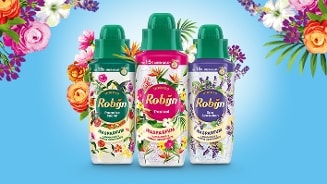 Drie flessen Robijn wasparfum in de geuren Paradise Secret, Tropical en Spa Sensation, omringd door kleurrijke bloemen op een blauwe achtergrond