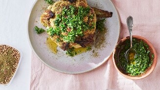 Geroosterde bloemkool met verse kruiden en specerijen, geserveerd op een bord met een zijkom van kruiden en een bakje gemalen specerijen.