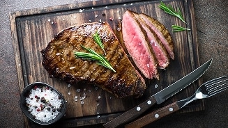 Gegrilde biefstuk geserveerd op een houten plank met rozemarijn en zeezout.