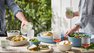 Glazen en schalen met eten en drankjes in een zomerse setting op tafel.