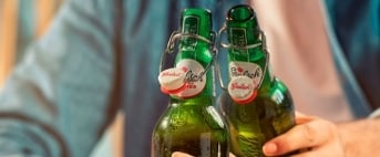 Twee personen proosten met Grolsch beugelflessenbier, met de NIX18-campagne duidelijk zichtbaar.