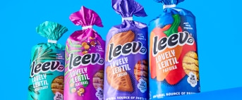 Vier zakken Leev Lovely Lentil koekjes in verschillende smaken op een blauwe achtergrond