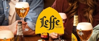 Verschillende glazen Leffe bier en Leffe bierflessen op tafel, omringd door mensen die samen genieten